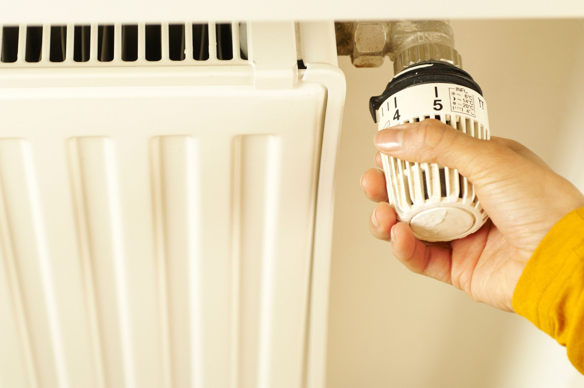 Nahaufnahme einer Hand, die das Heizkörperthermostat einstellt, um die Raumtemperatur zu regeln.