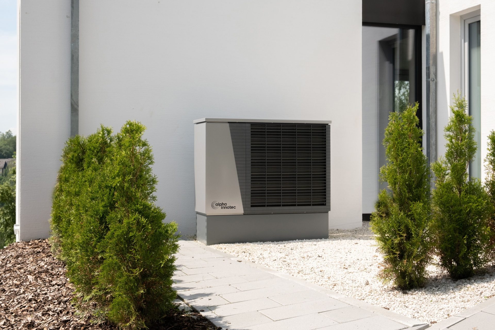 Ein Arbeiter installiert Solarmodule auf dem Dach eines Wohnhauses und fördert so saubere Energie. Außeneinheit einer Klimaanlage an einem modernen Gebäude, umgeben von Grünanlagen und Landschaftsgestaltung.