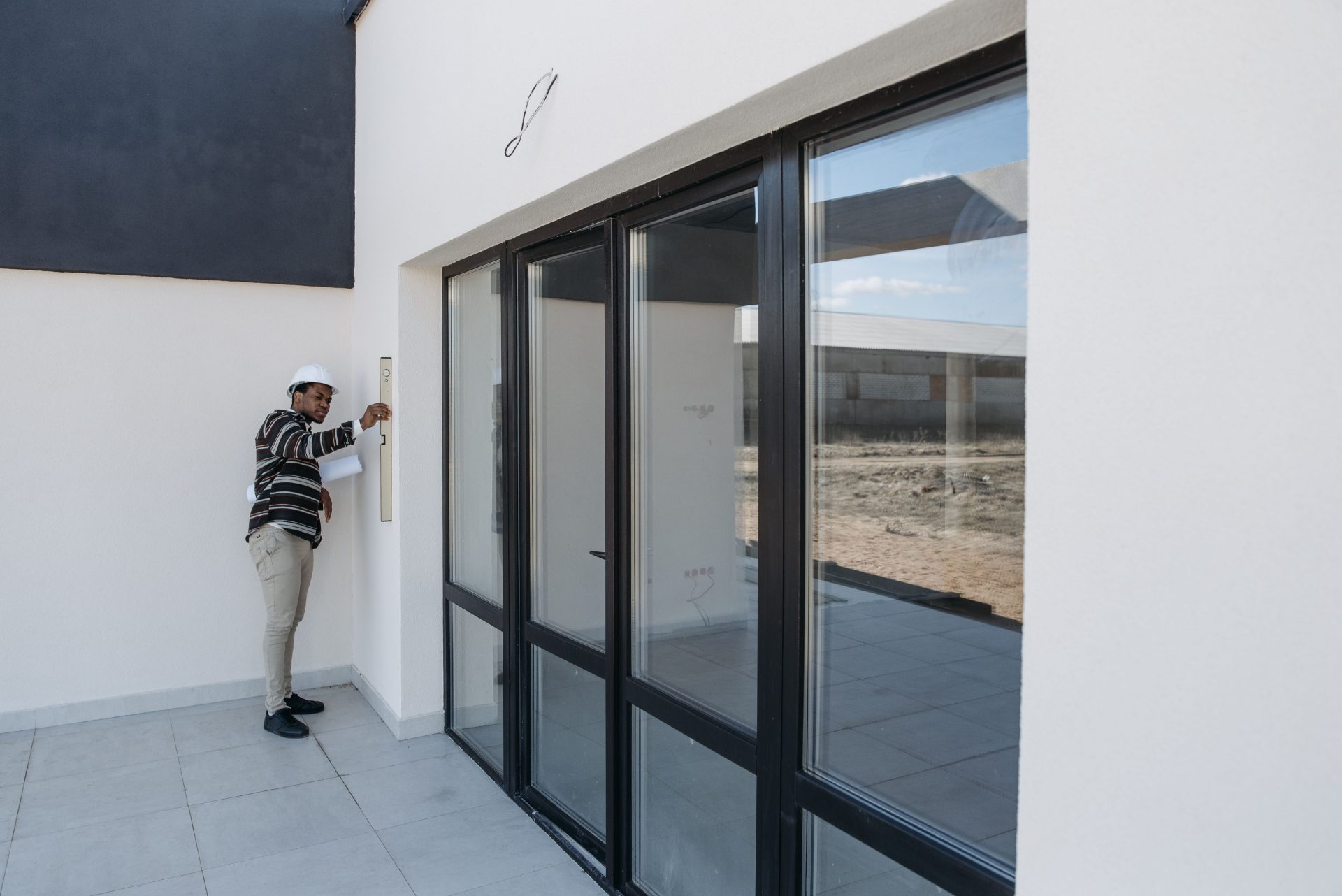 Architekt mit Schutzhelm begutachtet eine Glastür im modernen Hausbau.